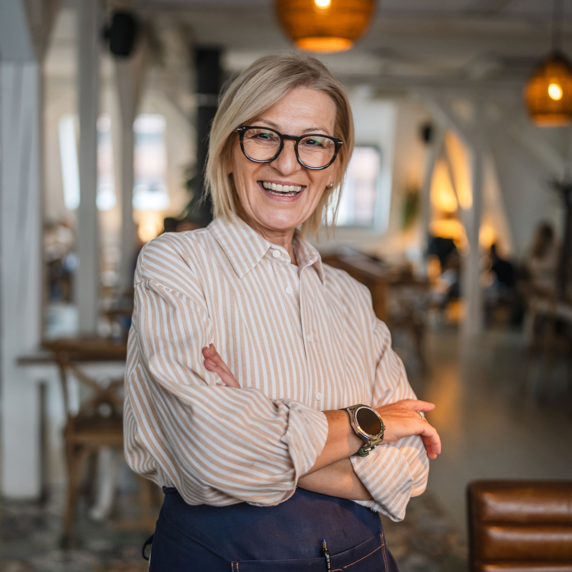 Portrait of a happy mature woman stand at restaurant arm crossed